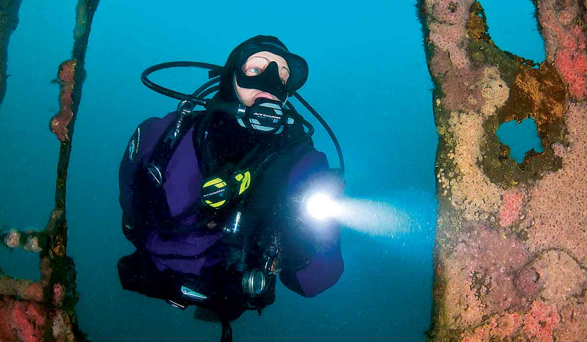 Diver cautiously enters a shipwreck while holding a light