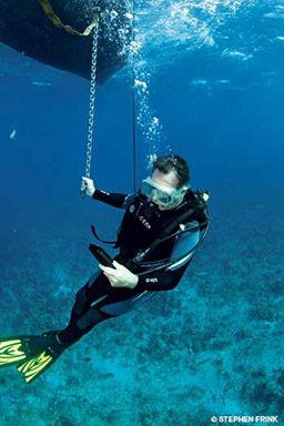Diver holds onto a chain and looks at dive computer