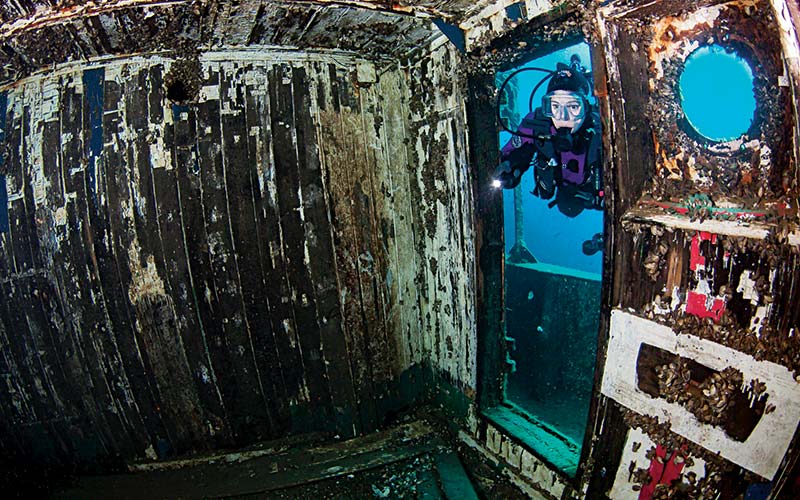 Diver in purple drysuit peers into a sunken ship