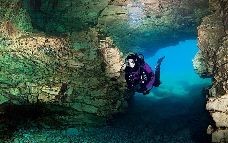 Diver in purple drysuit swims through a cave