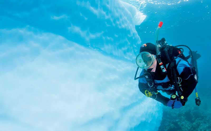 Diver swims along the face of an iceberg