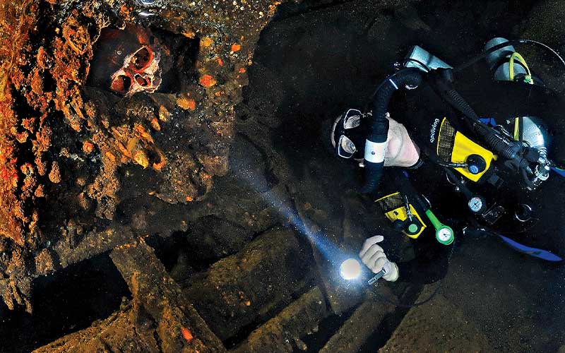Diver's torchlight brightens a skull in a shipwreck