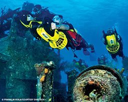 Divers use propulsion vehicles through a shipwreck