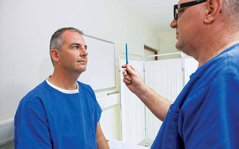 Doctor waves a blue pen in front of the eyes of a patient