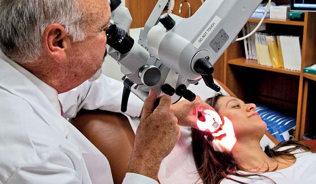 Ear doctor uses a contraption to look into the left ear of a female patient