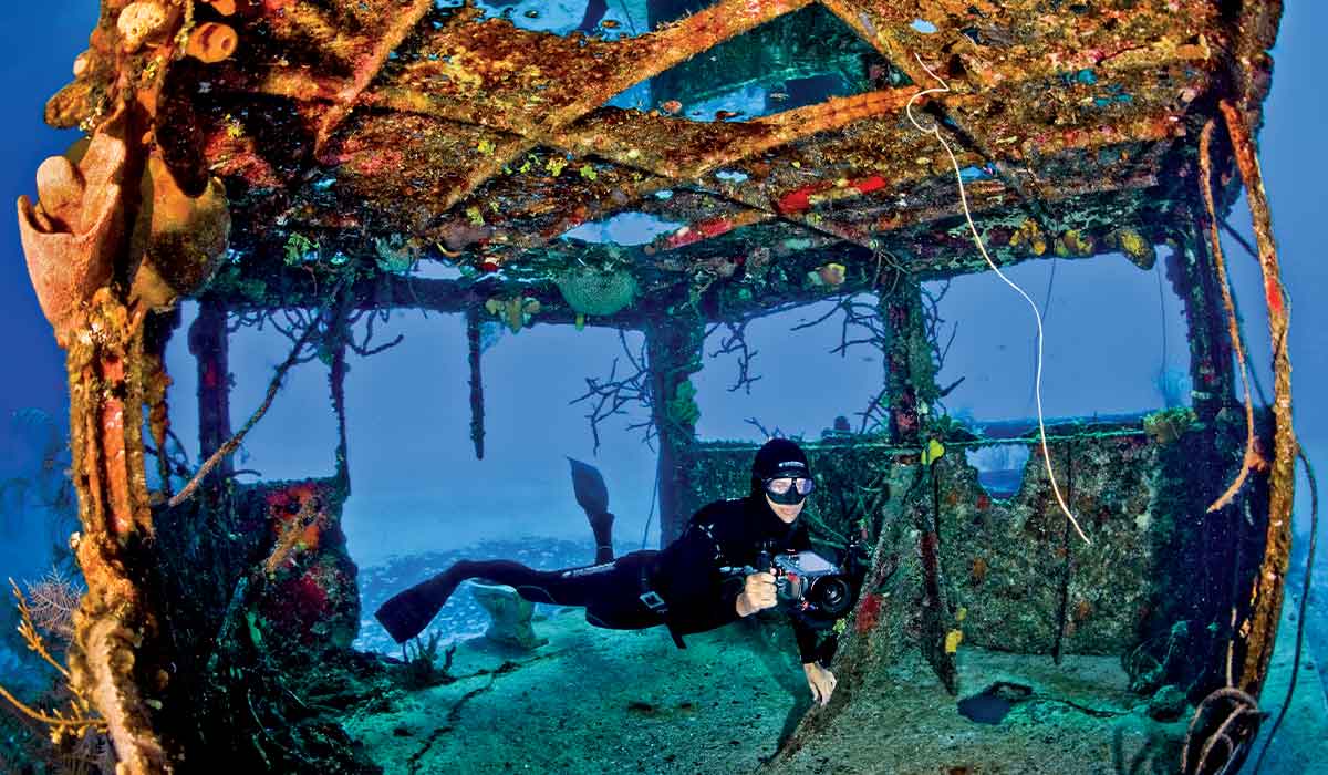 Freediver, holding a camera, swims through a wreck