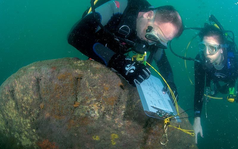 Diver archaeologists survey the wreck site near the starboard sidewheel.