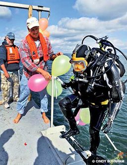 Male diver steps onto boat after a dive. Someone is holding balloons.