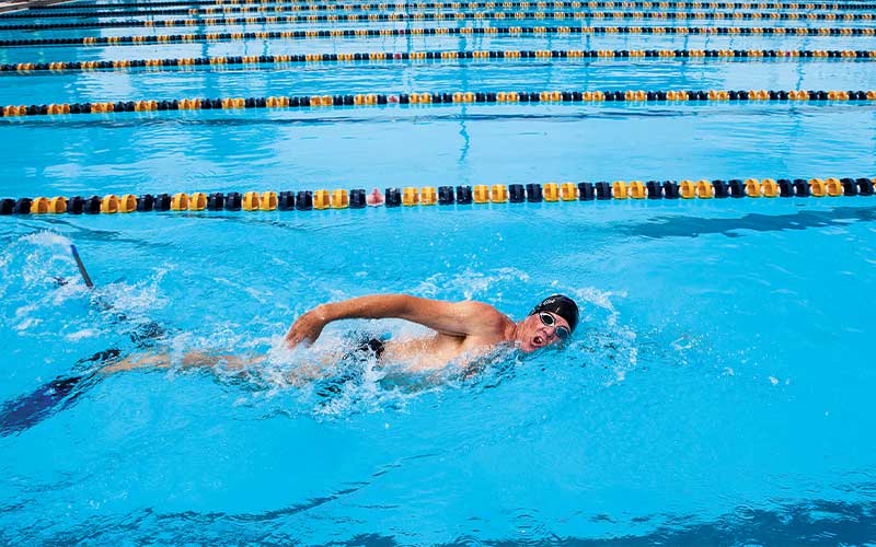 Man in Speedo swims freestyle in a pool lane