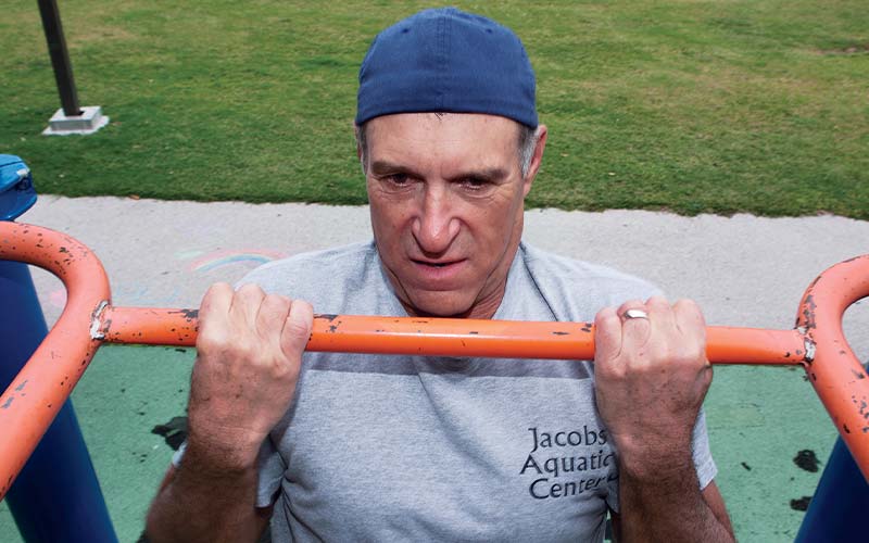 Man in backwards blue cap does a pull up on an orange bar