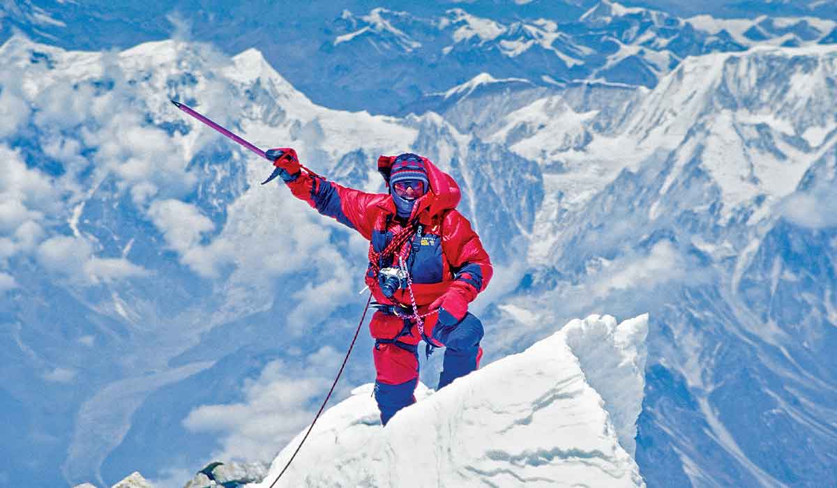 Man in red snowsuit is at the summit of a snow-capped mountain