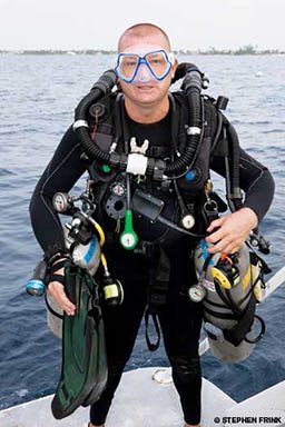 Nerdy-looking technical diver stands on a boat holding all the gear