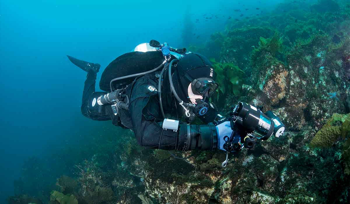Perfectly horizontal diver approaches a reef while holding a camera
