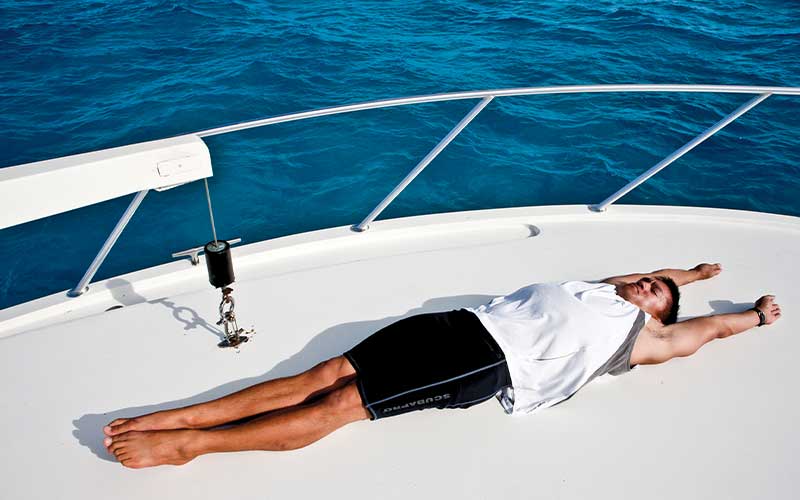Personal trainer lies face up on a fancy boat, with arms and legs fully extended