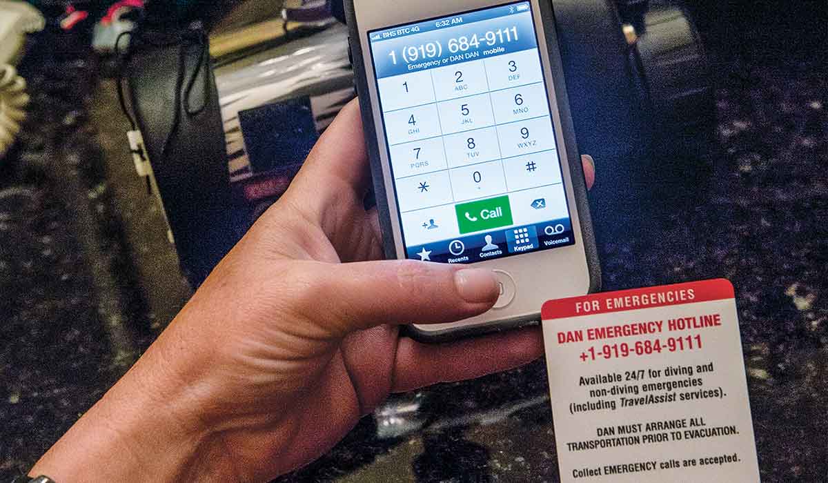 Person's right hand holds phone to call 911 and left hand holds DAN emergency card