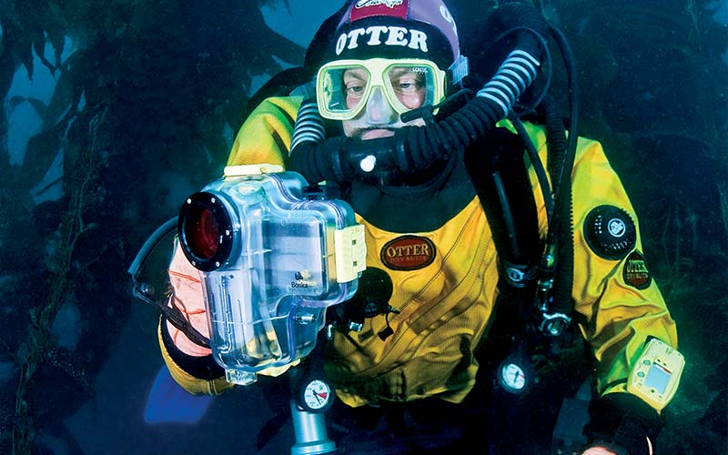 Rebreather diver in a yellow suit holds a camcorder