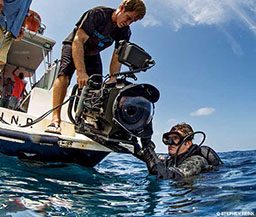 Scuba photographer is given camera from a man on a boat