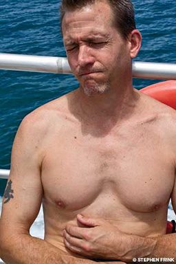 Shirtless man on boat holds his upset tummy
