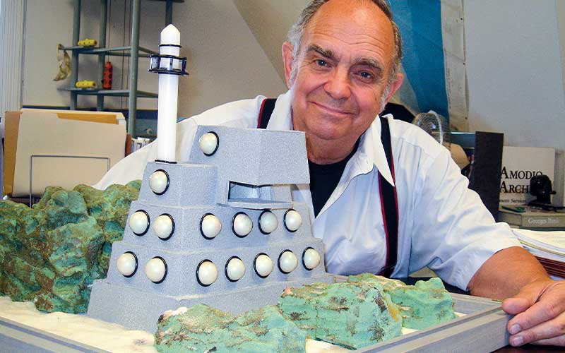 Smiling, bald man poses with a scale model of a building