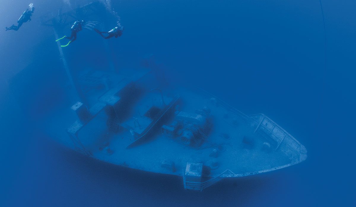 Three divers approach a sunken ship