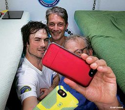 Three men cram together in a tight space to take a selfie