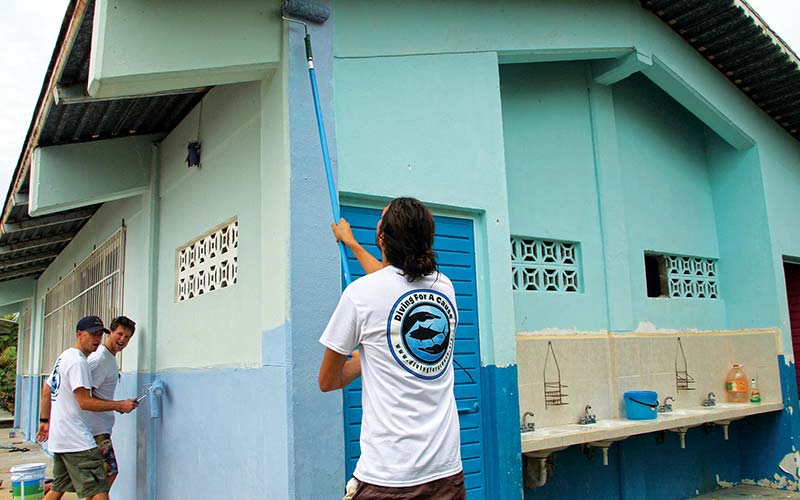 Three volunteers work together to paint a shack blue