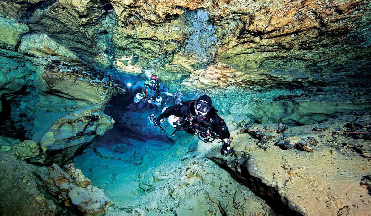 Two cave divers swim through a tight and craggy crevice