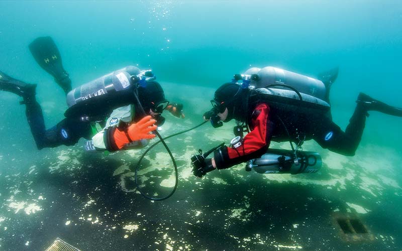 Two divers face each other and are sharing air