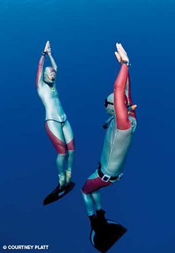 Two freedivers artfully swim toward the surface