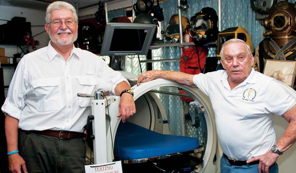 Two men stand next to a hyperbaric chamber