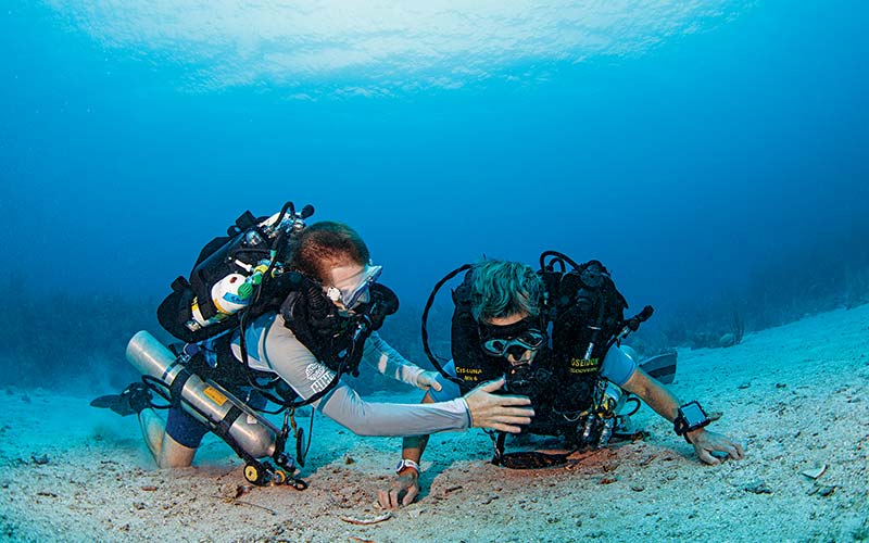Two rebreather divers work together at the bottom of the ocean