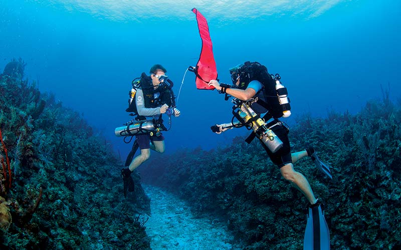 Two rebreather divers work together to deploy an emergency flag