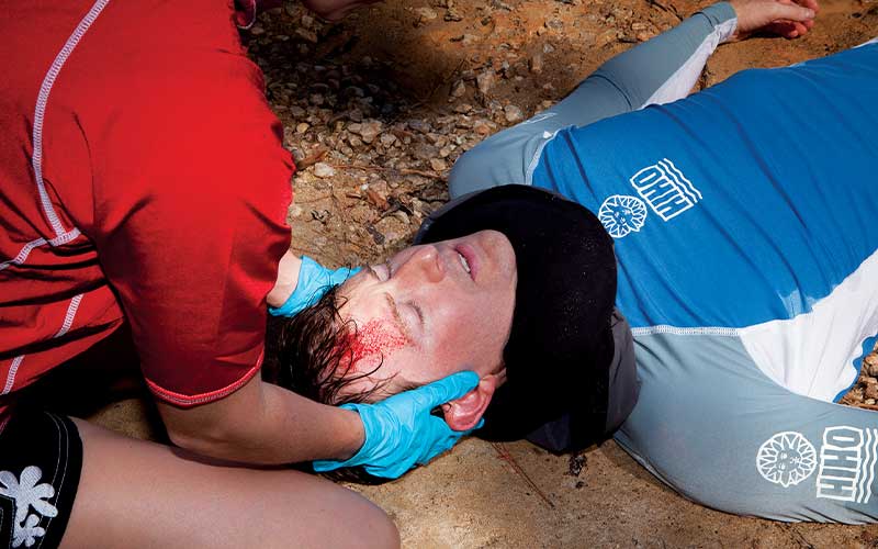 Unconscious man with bloodied forehead has an improvised collar around his neck to immobilize spine