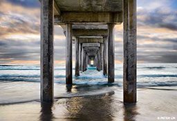 Underside of a pier at sunset with blue waves lapping at the posts