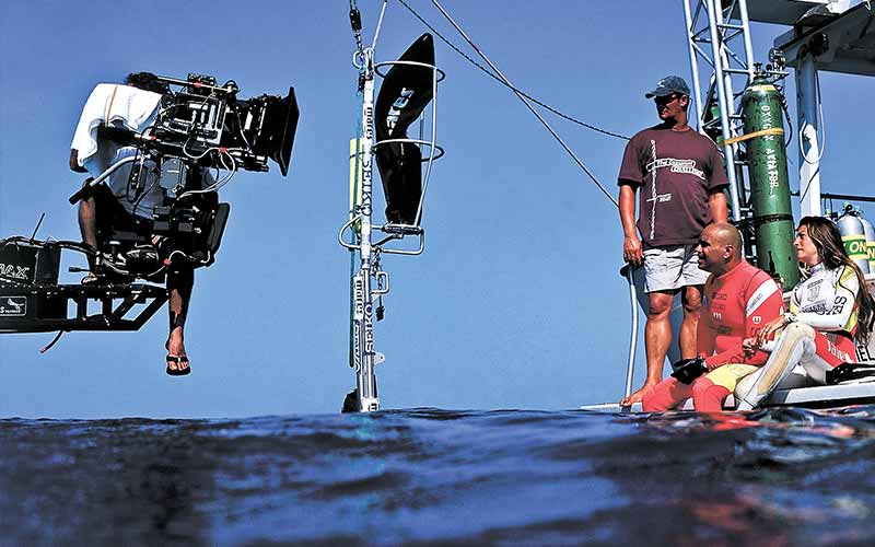 A film camera hovers over the water and is connected to a boat rig