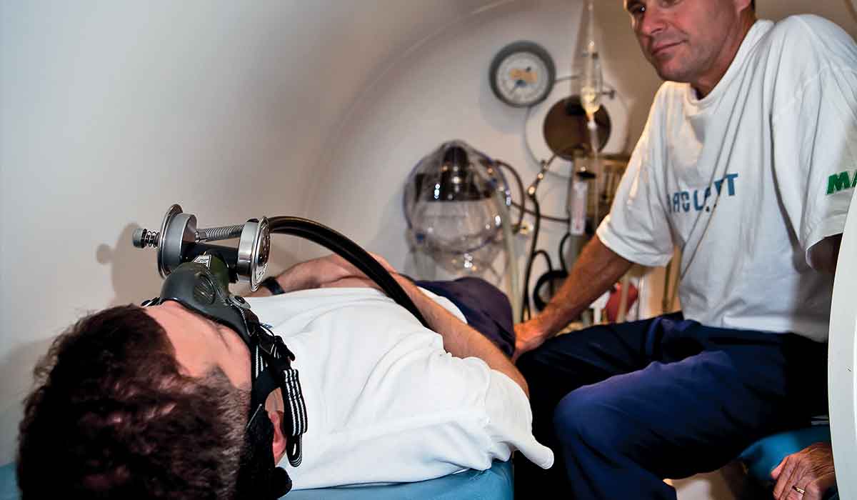 A man watches his friend as he receives hyperbaric treatments