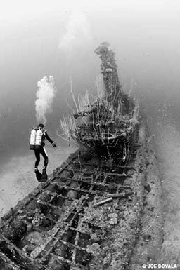 Black-and-white photo of lone diver approaching wreck