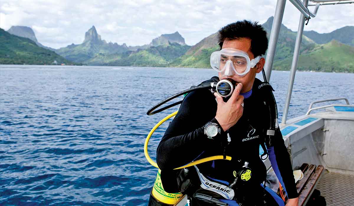 Black-haired diver is perched on side of boat and ready to get to dive site