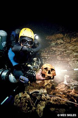 Cave diver in yellow helmet holds an old skull
