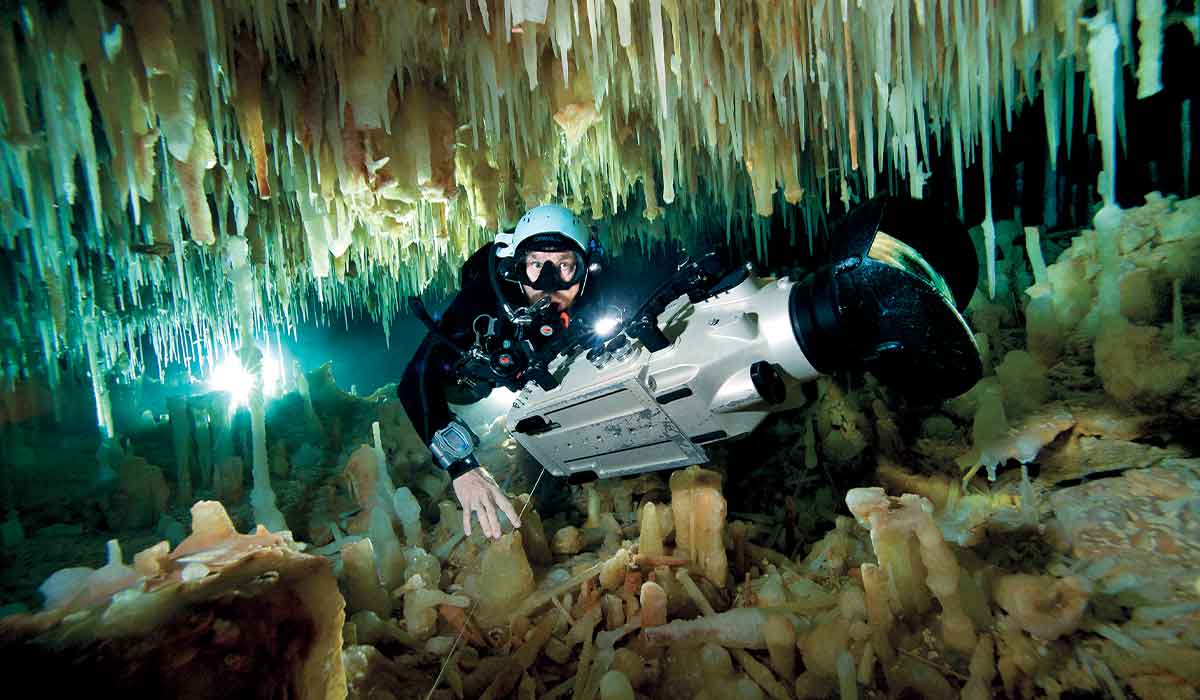 Cave diver swims through narrow stalactites holing a giant camera