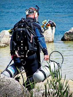 Diver walks toward the water carrying an air tank in each hand
