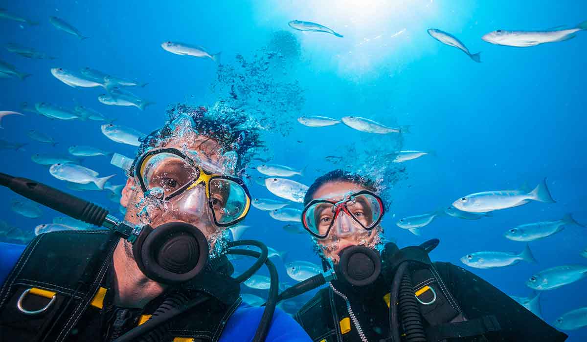 Male and female diver pose for a selfie in front of school of silver fish