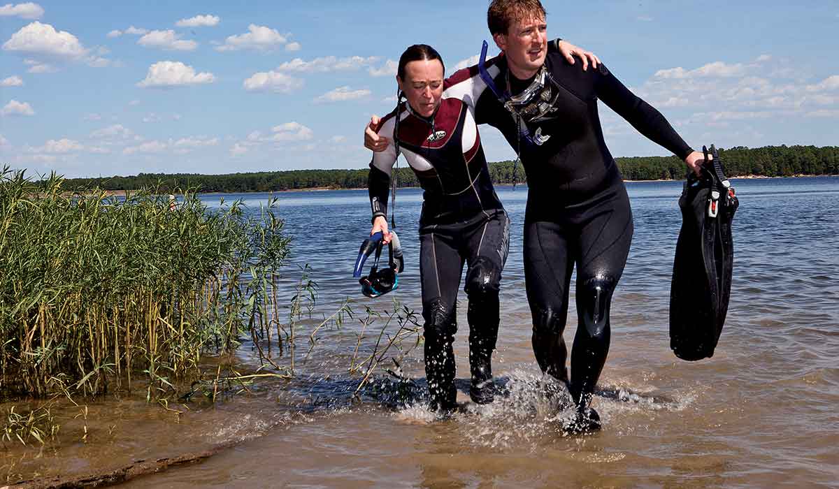 Male diver helps a limping female diver out of a lake to seek injury treatment