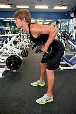 Male personal trainer is hinged forward, at hips, and is clutching weights at sides. His elbows are bent and high up, like he's going to row the weights