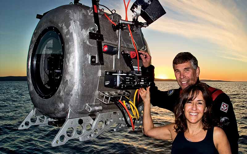 Man and woman pose landside with a hovering IMAX camera