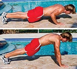 Man demonstrates push-up. First he's pressed down and then pushed up in plank position. He's not wearing a shirt just red shorts.