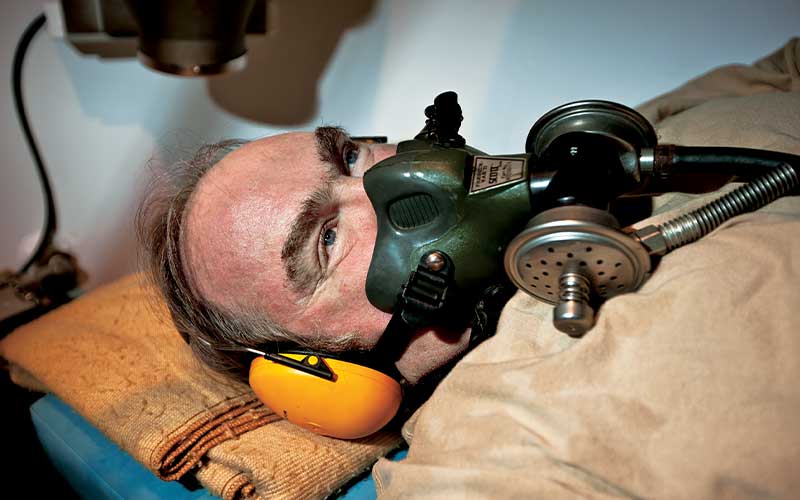Man lies on blue bunk wearing a hyperbaric mask