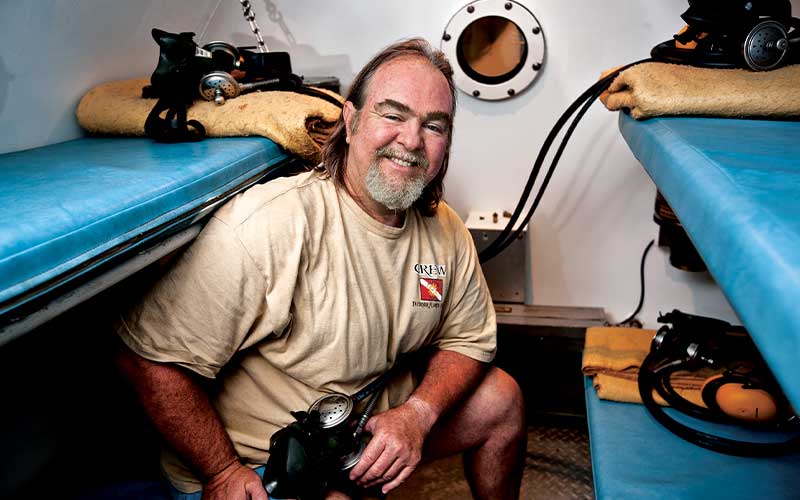 Man with beard sits on blue bunk in a hyperbaric chamber