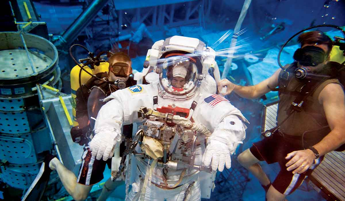 NASA astronaut is submerged in a pool and flanked by safety divers