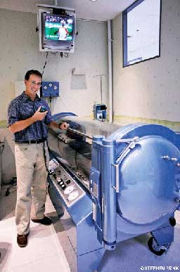 Nerdy man in glasses stands next to hyperbaric chamber